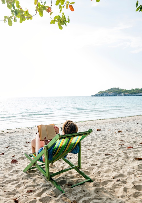 Woman reading a book on the beach in BLEAK HOUSE on the Beach: What Makes a Good Beach Read? | BookRiot.com