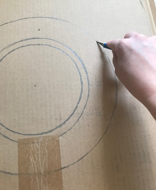 Picture of a hand holding a craft knife cutting out a cardboard circle