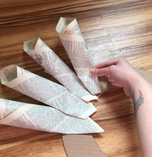 A picture of a hand placing a book page cone on a cardboard wreath