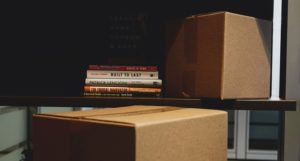 moving boxes near and around a book shelf with a stack of books