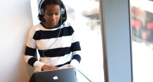 image of a woman in a striped black and white sweater and blue over-ear headphones; woman is using a MacBook https://unsplash.com/photos/mhmNmzxHBWs