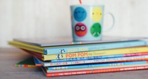 colorful stack of children's picture books with a kids cup in the distance