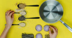 lay flat image of a sauté pan, spoons of spices, and vegetables against a yellow background https://unsplash.com/photos/oQvESMKUkzM