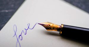 a black fountain pen on white paper next to the word "love" written in blue ink