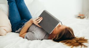 a photo of a woman reading in bed holding a book over her face