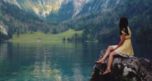 woman sitting on rock by beautiful lake