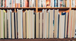 a photograph of books turned pages-forward, lined up in front of very full bookshelves; photo credit Jessica Ruscello via Unsplash