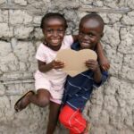two smiling Black children holding a cardboard heart
