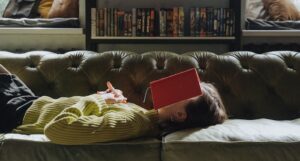 a photo of a woman lying on a couch with an open book resting on her face