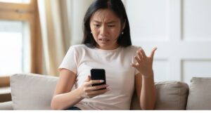 a woman reading her phone and reacting with a frustrated gesture and expression