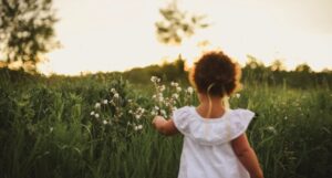 the back of a small child with brown skin picking flowers in a meadow