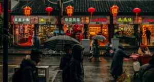 a photo of a Chinese street at night in the rain, with shops lit up and red lanterns hanging on a line
