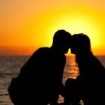 the silhouette of two people leaving in close to one another on a beach at sunset