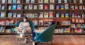 light-skinned Asian lady sits in front of a high book shelf in a book store