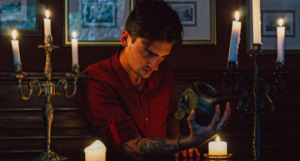 a young man with tattoos staring at a skull, surrounded by candles