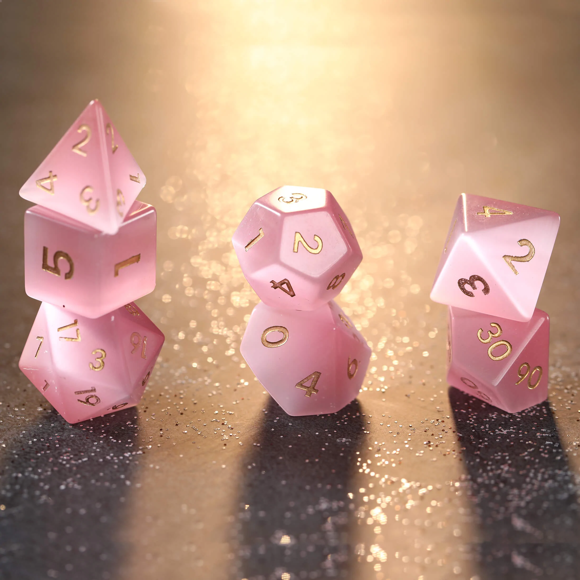 A photo of a set of seven pink dice with gold numbers on the faces. 