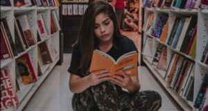 fair-skinned woman reading orange book on bookstore floor