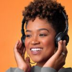 brown-skinned Black woman with headphones one; orange background