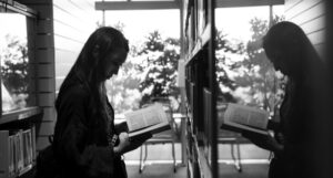 black and white photo of Asian woman reading by a window that is reflecting her image