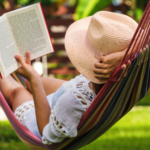 a photo of someone wearing a floppy hat and reading in a hammock