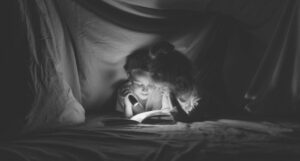 a young goy and girl reading by flashlight