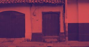doors on a street in Latin America. The roof of the structure is red tile and the walls are cracked, and the image is bathed in an ominous red filter
