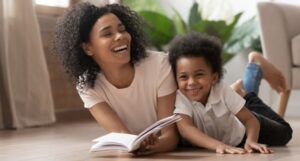 Black adult and child reading a book and laughing