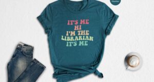 T-shirt with retro rainbow colored text reading "It's me Hi I'm the librarian it's me"