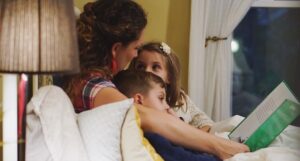 a photo of a woman in bed reading with two kids