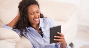 brown-skinned Black woman with long hair smiling and holding an ereader
