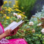 light-skinned woman of color reading in a pink dress in a garden