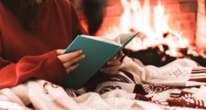 a photo of a person reading in bed under a blanket with a fireplace in the background