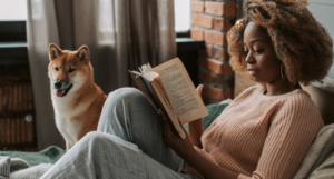 a photo of a Black woman reading in bed with a dog beside her