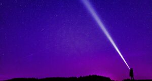 a person shining a bright flashlight into a purple and pink star-filled sky