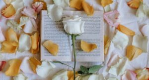 an open book with a rose and rose petals strewn about it