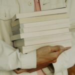 a closeup photo of someone carrying a stack of books