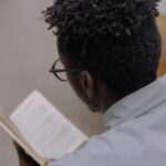 dark brown-skinned man reading a books; pic from the bac