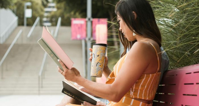 a light-skinned Asian woman reading a book on a pink bench