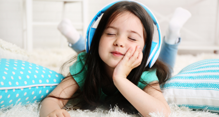 a photo of a kid with light skin and long hair closing their eyes, listening to headphones