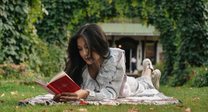 light-skinned Asian woman laying on a blanket on the grass and reading