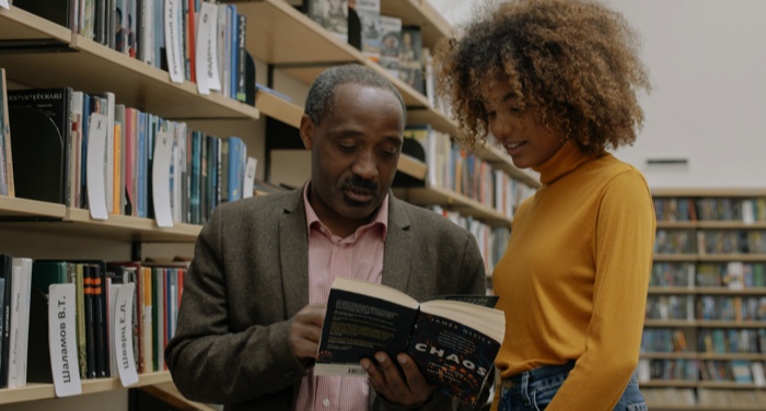 a Black man and young woman discussing a book in a library