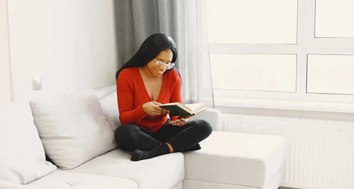 a brown-skinned Black woman sitting and reading a book