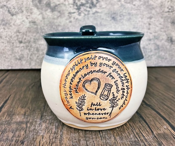 white and navy blue clay mug with a quote from Practical Magic on one side along with drawings of a salt shaker, a sprig of rosemary, a sprig of lavender, and a heart