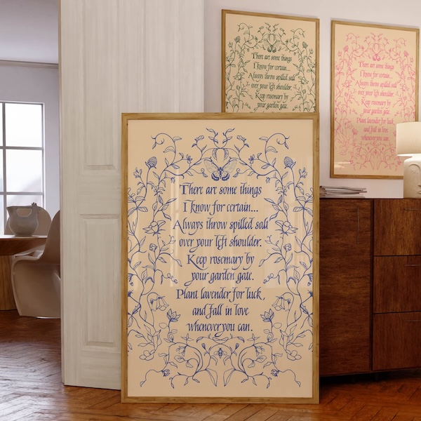 large wall hanging of a quote from Practical Magic bordered by flowers and vines in purple ink. Hanging on a wall behind it are two versions of the piece in green and pink ink