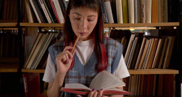 A light-medium skinned Asian Woman with Red Hair highlights Reading a Book at the Library