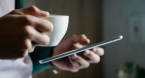lighter skinned hands holding a mug and tablet