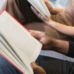 the hands of two people with different skin tones reading books