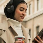a light tan-skinned woman with a headscarf looking at her phone while wearing headphones