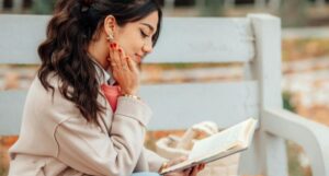a lightly tan-skinned woman sitting pleasantly reading a book while sitting on a bench (1)