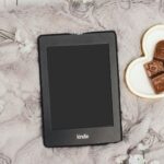 kindle on gray blanket with heart-shaped plate of chocolates nearby